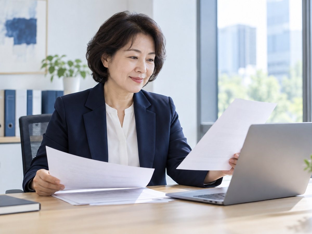 PG사 · 여성이 서류를 들고 노트북 앞에서 확인하는 장면(연출 사진)